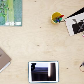 View down onto a tabletop with a ipad, notebooks, pens and publications on it.