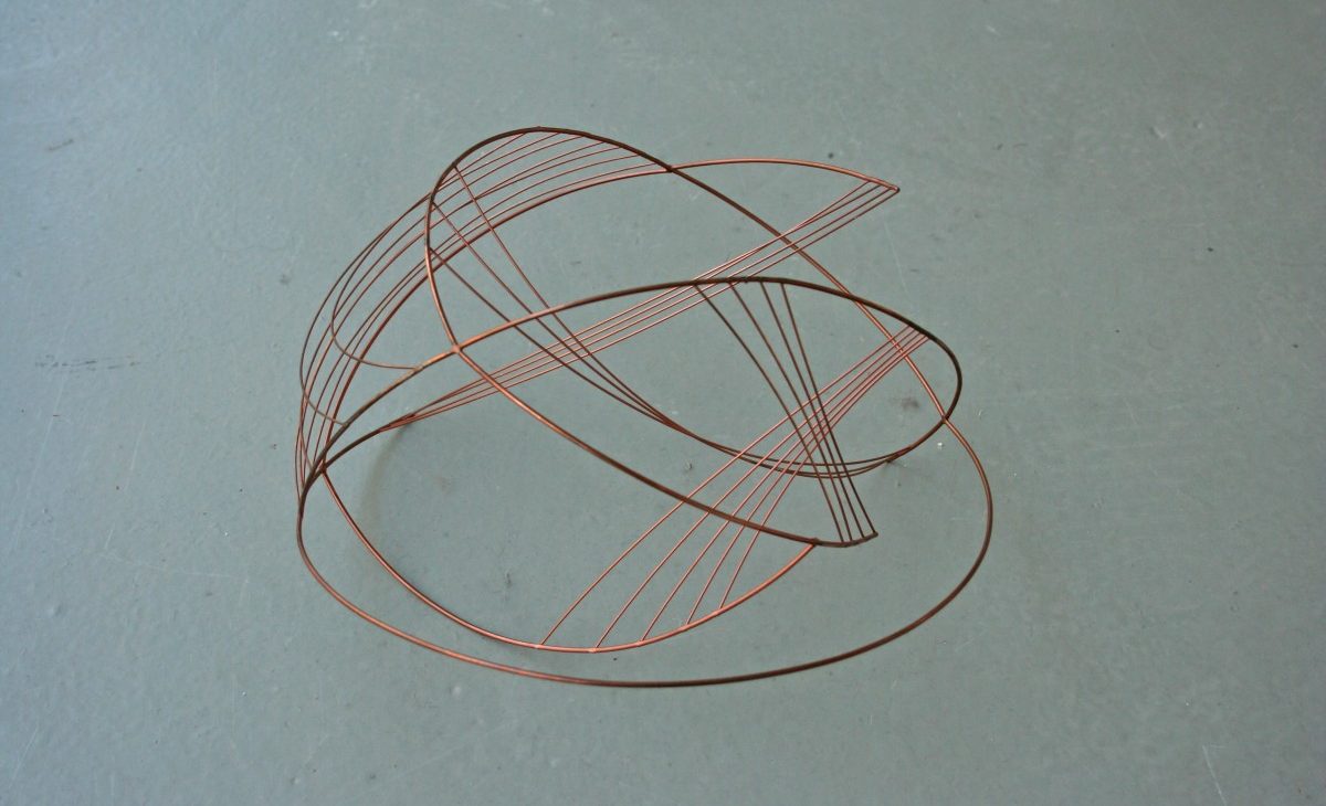 An abstract copper wire sculpture constructed from loops and lines is displayed on the floor