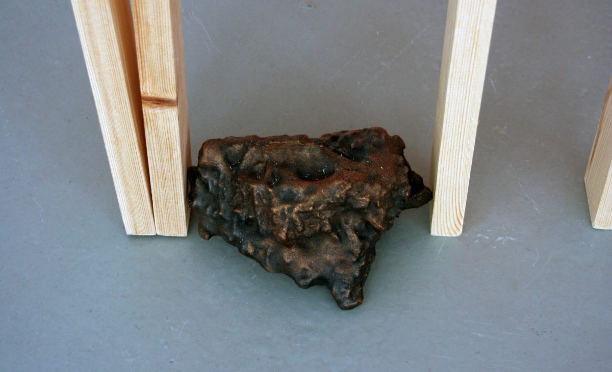 Close up of a bronze casted rock between wooden lengths, displayed on the floor