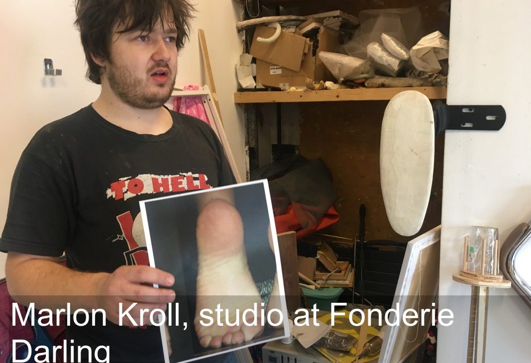 Artist Martin Kroll in his studio holding up a photograph of a foot