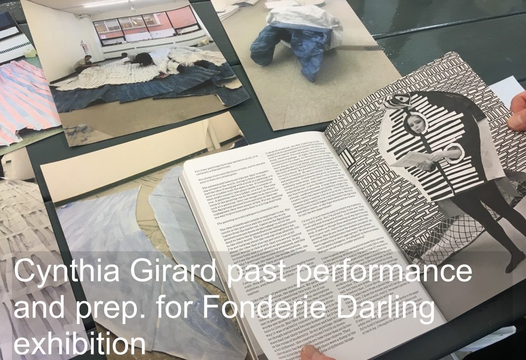 Artist Cynthia Girard holds open a book showing a past performance; there is past prep and photographs on the table