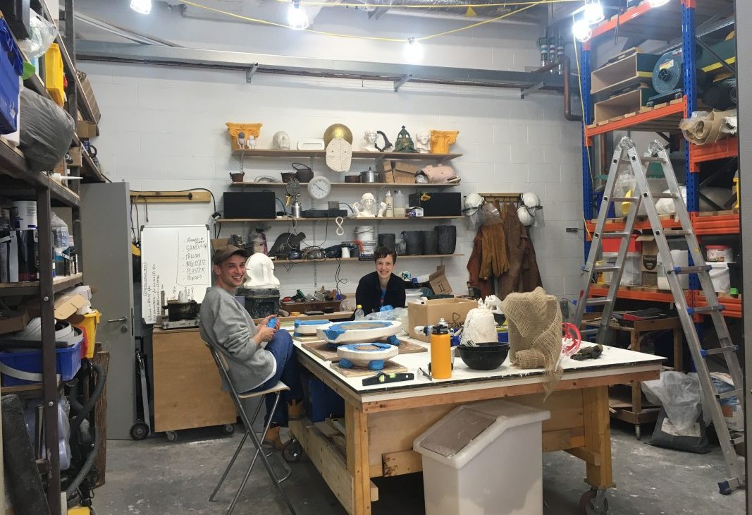 Two artists in conversation, sit at a large white work table, making plaster jackets for mould making