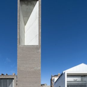 Tall brick tower with large open window viewing into angular interior concrete space