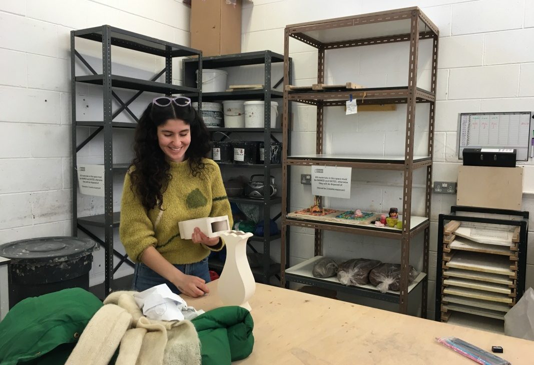 Artist Mina Heydari-Waite in foreground holding two recently fired artworks, white stoneware vases made from slip cast moulds