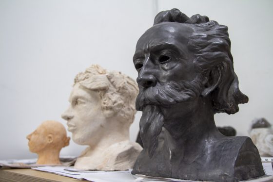 Three moulded head sculptures on a shelf in black, white and orange coloured materials