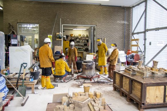 A team in protective clothing working on an aluminum pour, standing around the furnace.