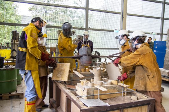 A team in protective clothing working on an aluminum pour, liquid metal being poured into the mould.