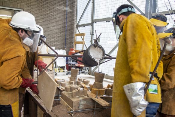 A team in protective clothing working on an aluminum pour, liquid metal being poured into the mould.