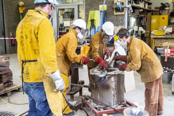 A team in protective clothing working on an aluminum pour, standing around the furnace.