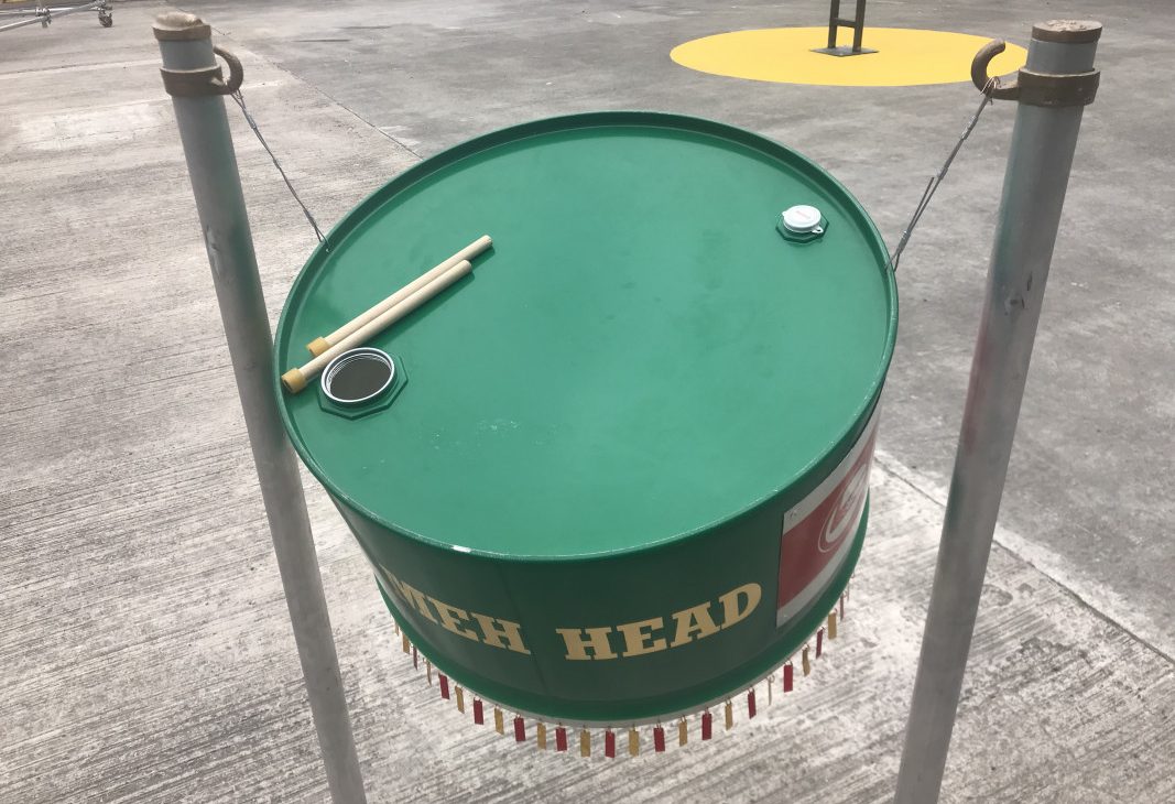 Green painted oil drum suspended so that visitors can play it like a steel pan drum, with two beaters on the top part of Ashanti Harris exhibition