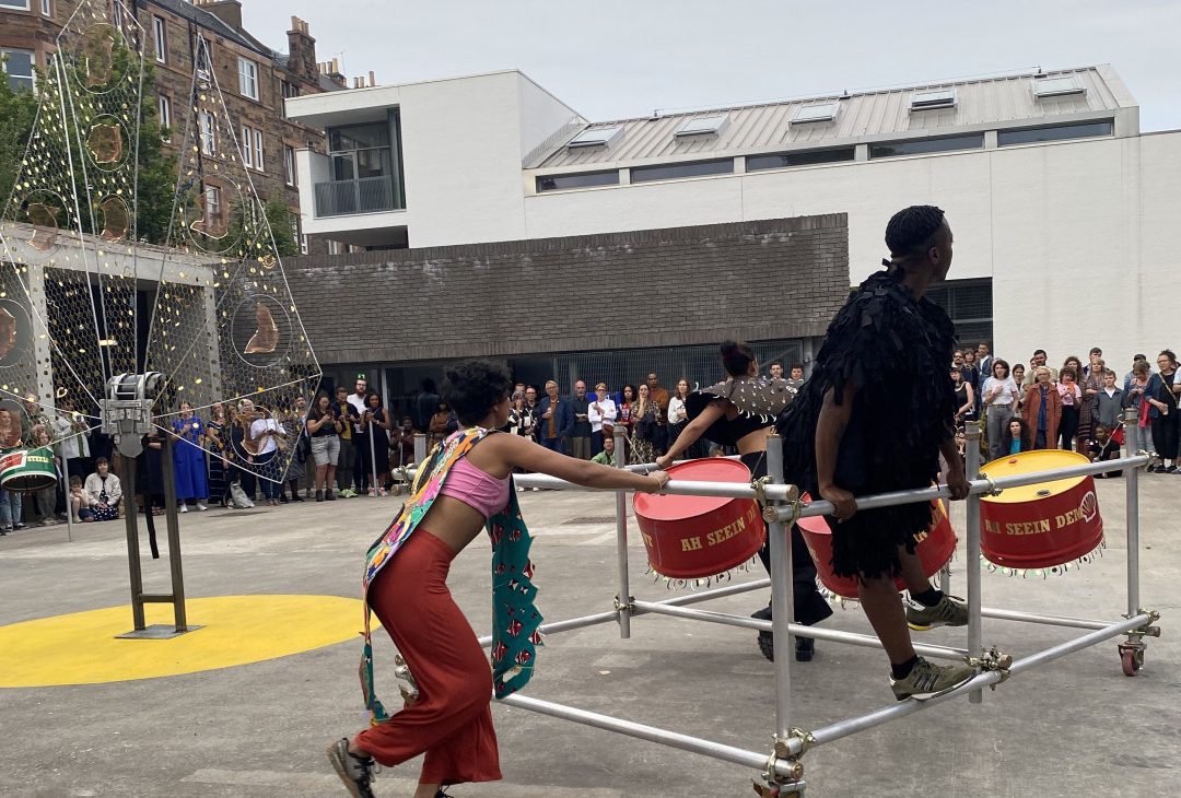 Performers pushing a scaffolding float within a courtyard, Ashanti Harris exhibition