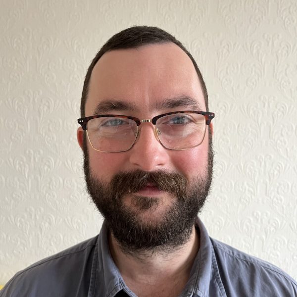 Portrait of Chris Coatham wearing a grey shirt and glasses.