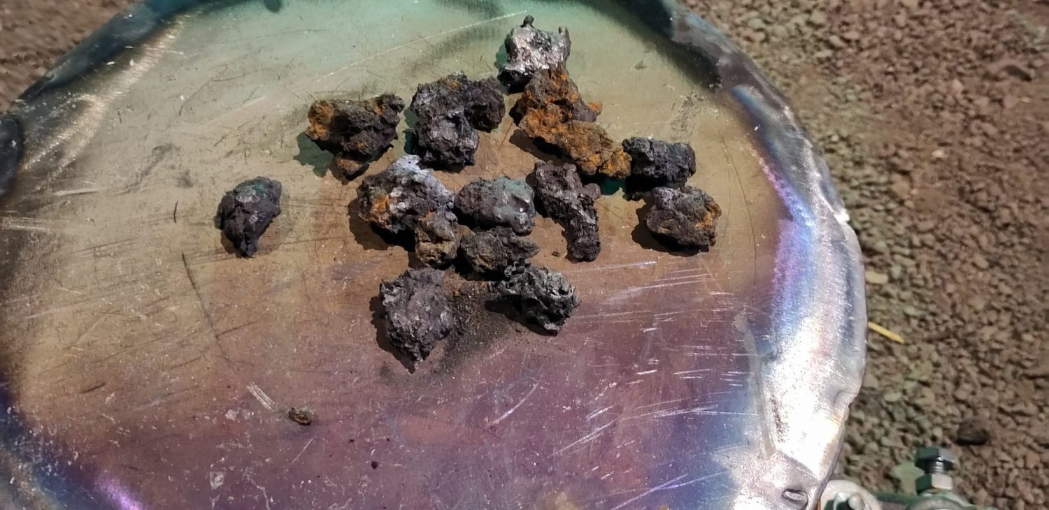 Small nuggets of iron ore on a polished metal surface.