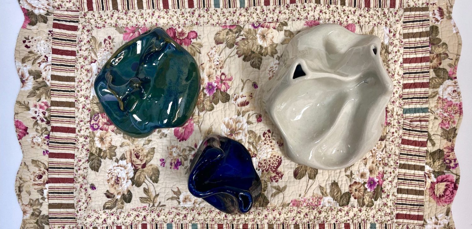 Three ceramic sculptures in deep white, green and darker glaze on a textile mat, viewed from above.