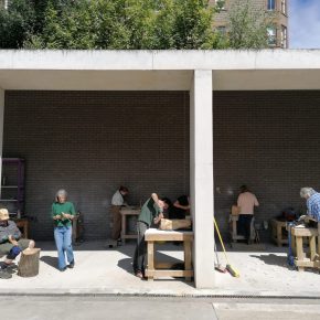 Several people working in the bays of a sunny courtyard with wood blocks and work tables.