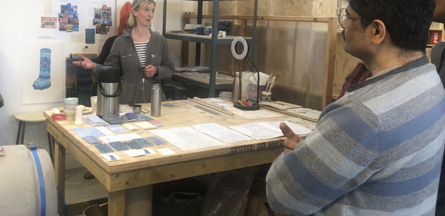Project Space Holder Claire Duffy standing behind a large pine work table with drawings and test tiles laid out on it, speaking to tour visitors.
