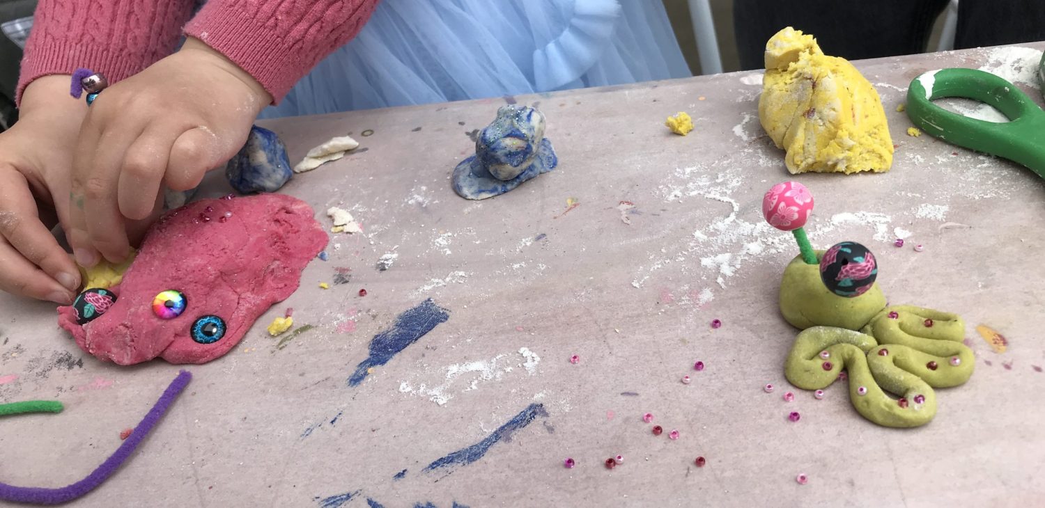 A child's hands working on pink and yellow salt dough or plasticine on a wooden surface.