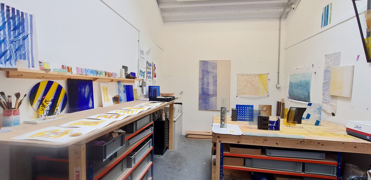 Jack Brindley's studio showing two work tables and yellow, blue and turquoise glass works.