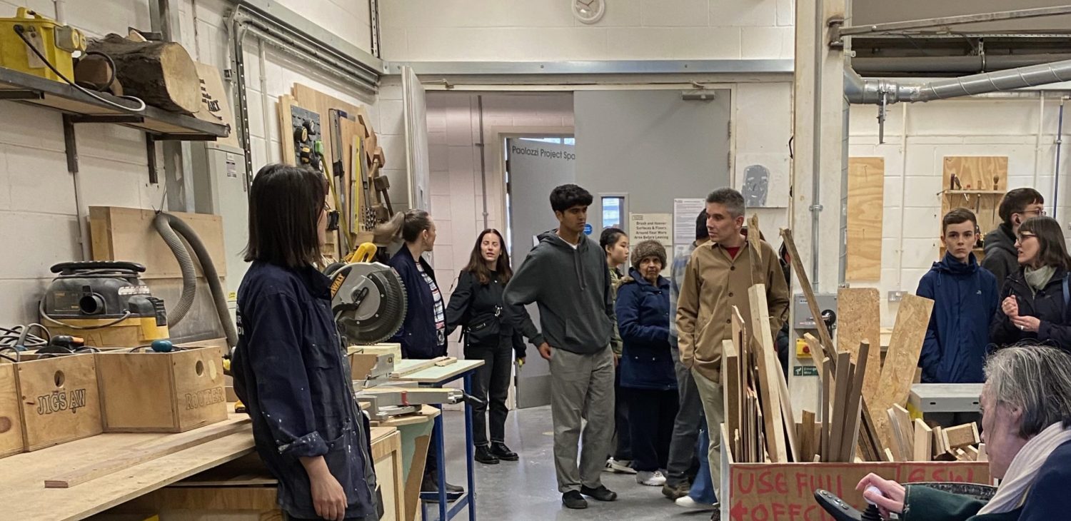 A group of people standing in the Wood Workshop as part of a tour with staff member Emma Hislop.