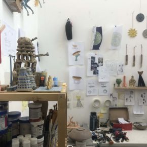 Studio photo shelves with materials and items, and drawings on the facing wall above a desk