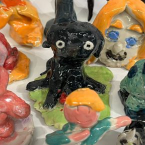Glazed ceramic figurines, including a wide-eyed black dog on a green base, a dabbing figure in teal and orange, and other colorful sculptures with playful, abstract forms.