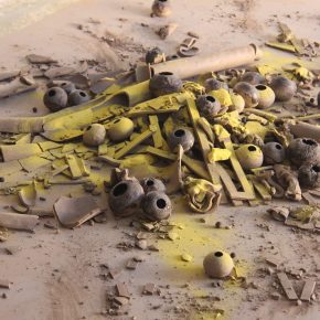 Artwork by Simon Lee Dicker, which includes broken/fragmented ceramic pieces on the floor with yellow pigment.