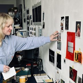 Natasha Cox reaching over to images on her studio wall, 2026.