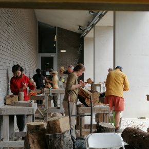 Group of participants carving timber with mallets and chisels at outdoor workbenches during a wood carving course at ESW.